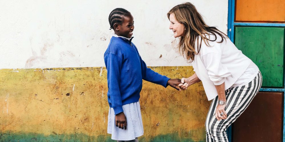 Lotte and student in Kenya holding hands near colourful wall